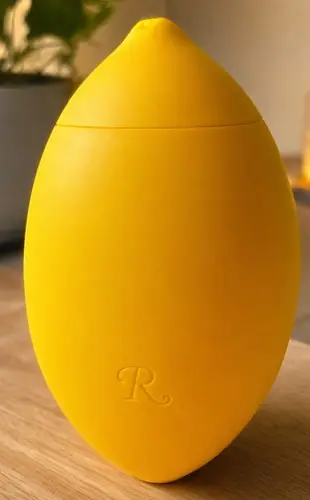 Rumeni klitoralni masažer Lem v obliki limone, postavljen pokonci na površini.