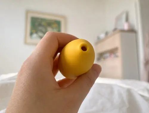 Stranka drži živo rumeni klitoralni masažer Lem v roki.